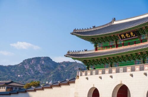 View of Gyeongbokgung Palace with traditional Korean architecture set against a mountain backdrop on a sunny day.