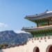 View of Gyeongbokgung Palace with traditional Korean architecture set against a mountain backdrop on a sunny day.