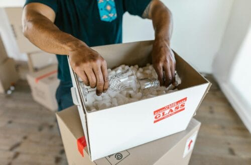 Person packing glassware into boxes with packing peanuts, preparing for relocation.