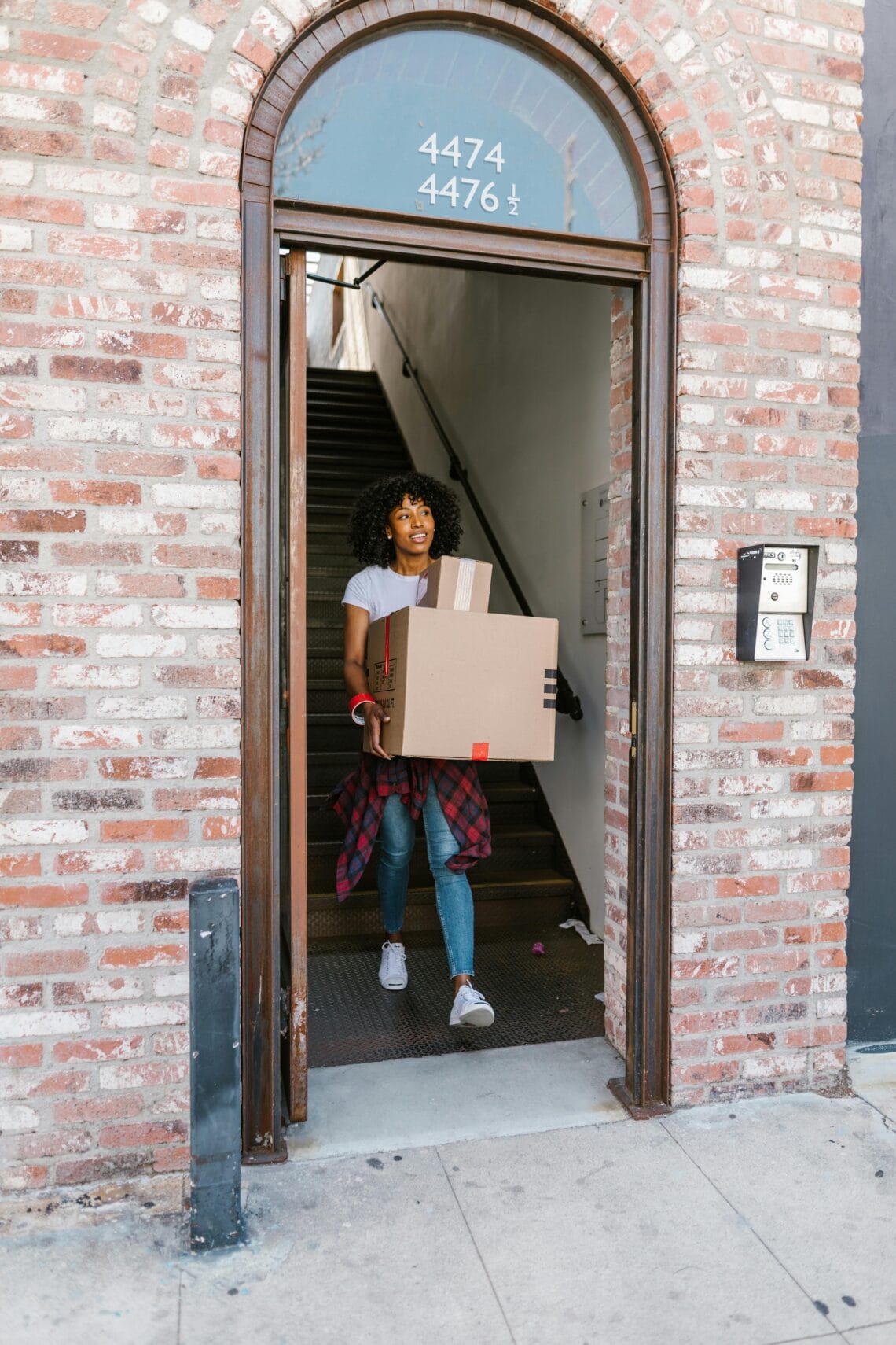Young woman moving boxes out of an apartment building. Ideal for relocation and moving day themes.