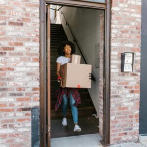 Young woman moving boxes out of an apartment building. Ideal for relocation and moving day themes.