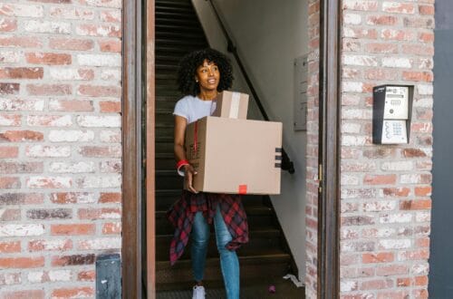 Young woman moving boxes out of an apartment building. Ideal for relocation and moving day themes.