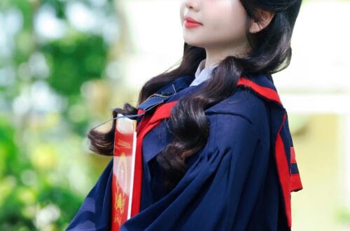 Portrait of a young graduate in a cap and gown with diploma in hand, outdoors in a lush garden.